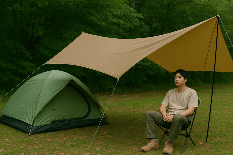 小川張りスタイルのタープの下で、日本人キャンパーがアウトドアチェアに座りくつろいでいる様子