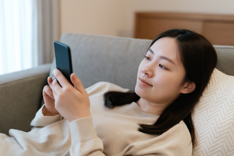 日本人女性がソファーに寝転んでレビューをスマホで見ている様子の画像