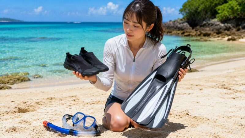 足裏を保護するマリンシューズと水中で推進力を得るフィンを比較する女性。