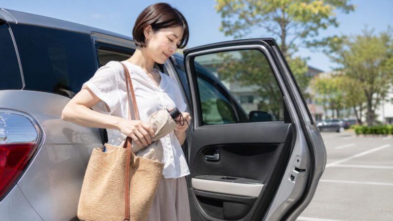 車の乗り降りで折りたたみ日傘をバッグに収納する女性