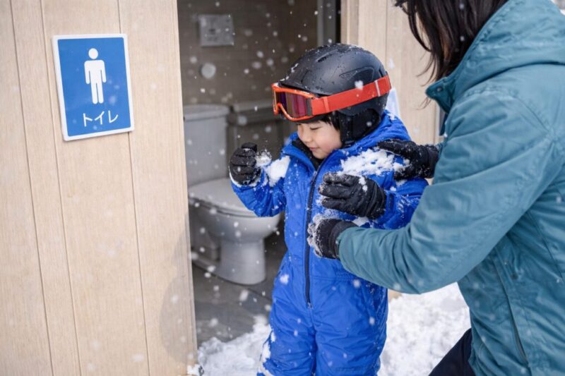 トイレに入る前に、上着の雪を払ってから脱ぎ着の準備をする親子の様子