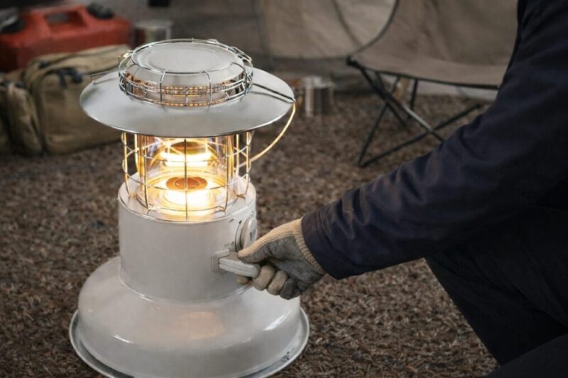 テント内で手袋をした手が点火用ハンドルを回し、ストーブに火が入った様子