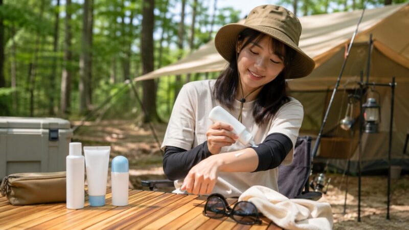 キャンプ場で日焼け止めを腕に塗りながら外遊びの紫外線対策をしているイメージ