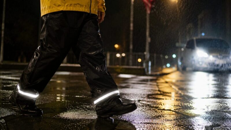 夜の雨道で黒いレインパンツの反射材が光り、足元の視認性を高めている様子