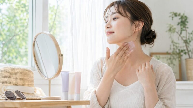鏡を見ながら首元までUV下地をなじませて自然な仕上がりを確認する女性のイメージ
