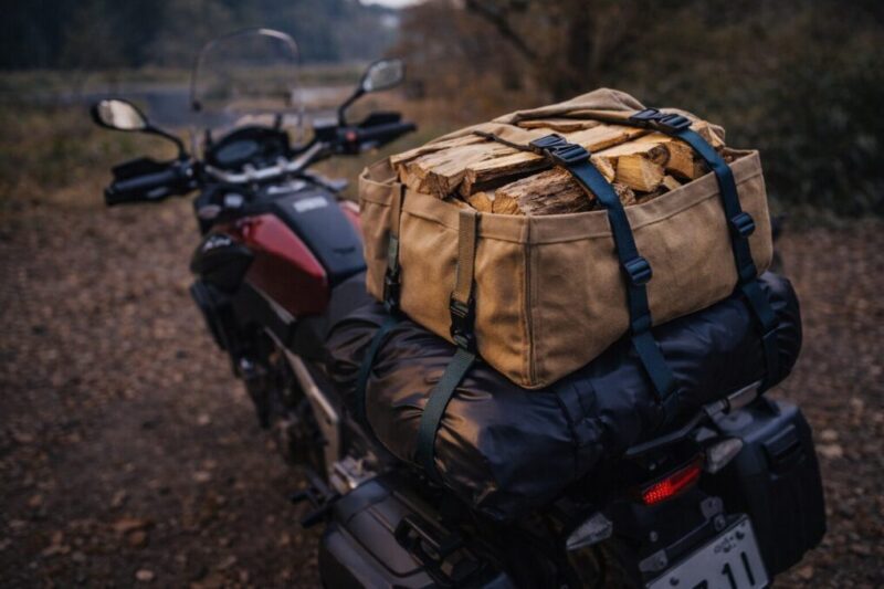 バイクの荷台に防水バッグと薪バッグをベルトで固定し、濡れにくく安定して運ぶ積載イメージ