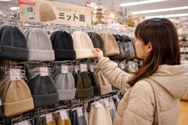 100円ショップの冬小物コーナーでニット帽を手に取って選んでいる様子