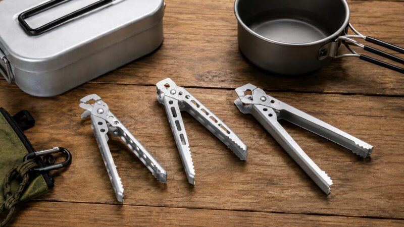 形や長さの違う3種類のクッカークリップを木製テーブルに並べ、メスティンや小型鍋との相性を比較している様子。