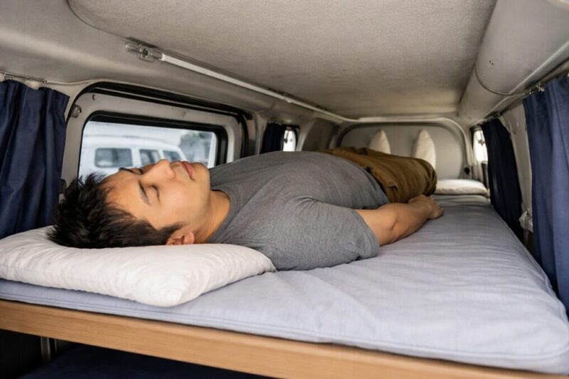 軽バンの車内で高すぎるベッドに横たわり、頭上の狭さが目立つ失敗例のイメージ