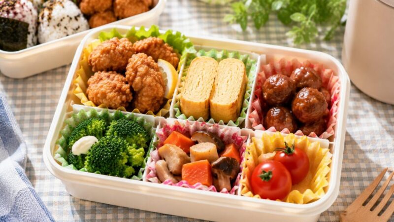 唐揚げや卵焼き、ミートボール、ブロッコリーを仕切りカップで分けて詰めた弁当箱
