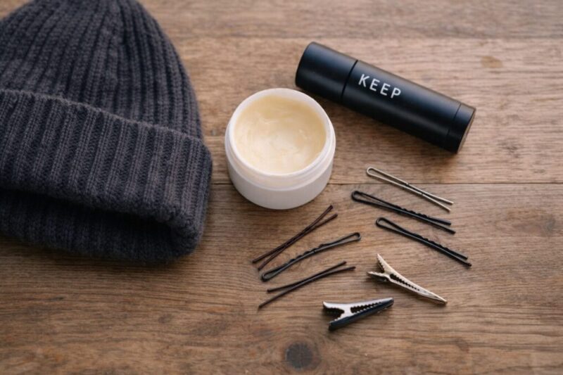 ニット帽の横にヘアピンと整髪料を並べ、前髪を固定する準備をしているイメージ写真