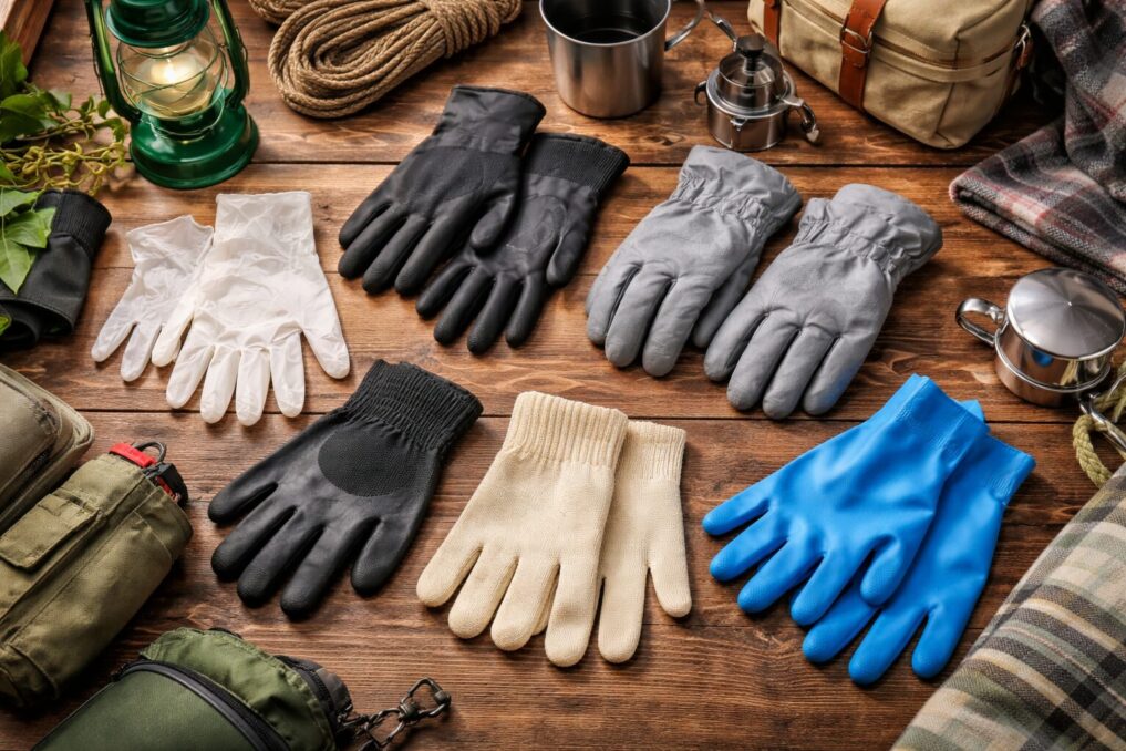 木目のテーブルに複数タイプの手袋とキャンプ小物を並べ、用途別の選び分けをイメージできる写真