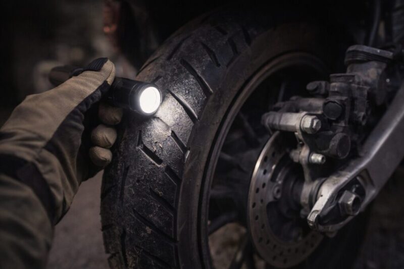 中古の125ccバイクを選ぶ前に、タイヤの溝やブレーキ周りの消耗をライトで確認している様子