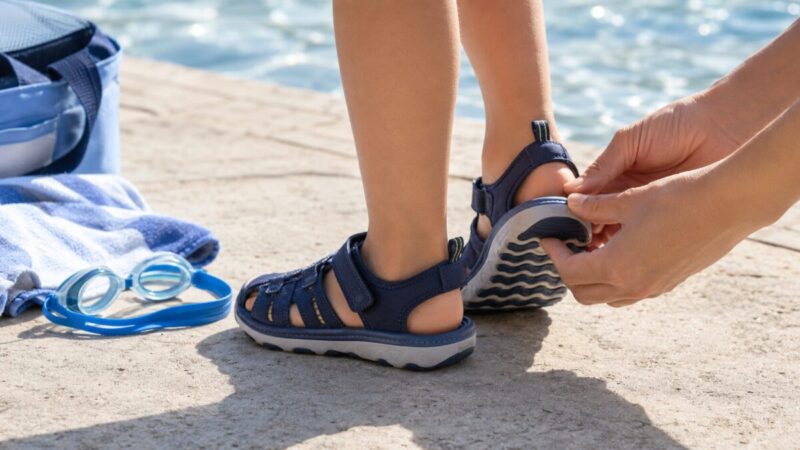 子ども用のストラップサンダルを履いた足元を大人が確認し、かかとのホールド感や靴底の滑りにくさを見ている画像
