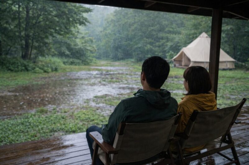 小雨のグランピング施設で屋根付きデッキから景色を楽しむ二人