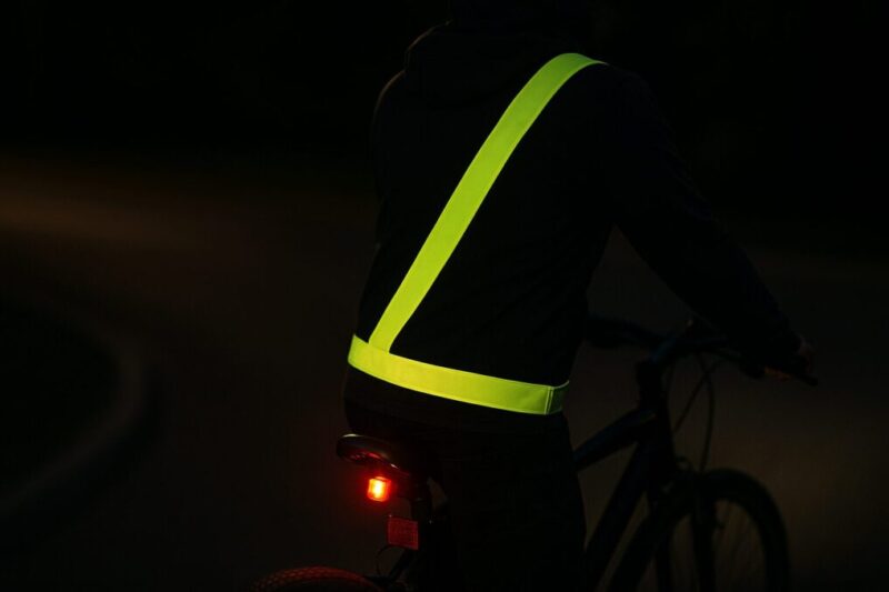 後部リフレクターと尾灯を備えた自転車に乗り、反射タスキも着用したライダーの安全な夜間走行イメージ。