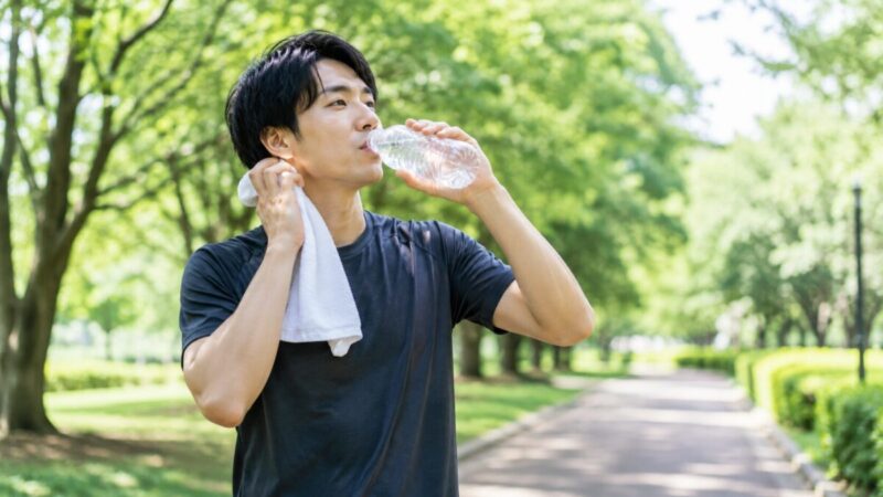 汗を拭きながら水分補給してウォーキングを続ける男性