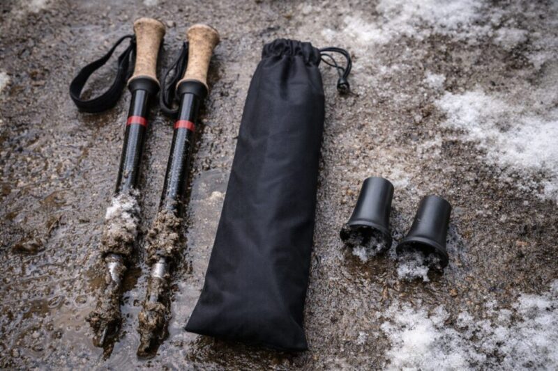 泥と雪で汚れたトレッキングポールと、収納袋・先端カバーを並べた後処理のイメージ