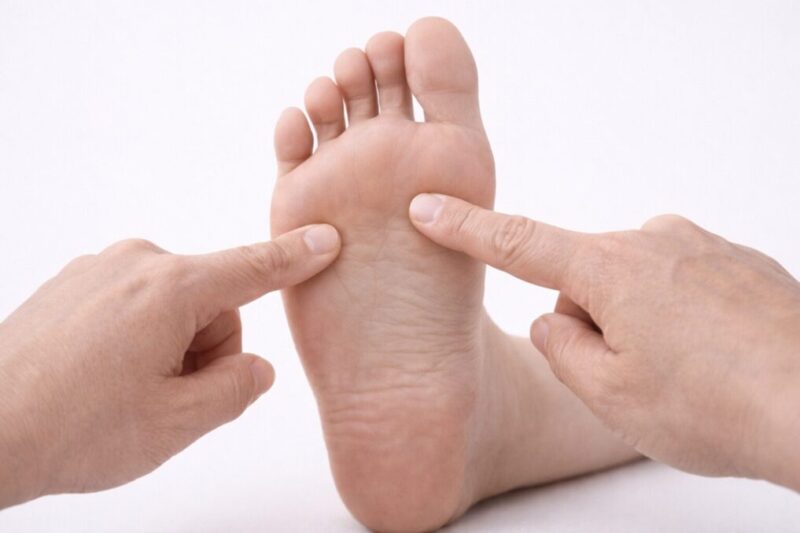 足裏のかかと・土踏まず・つま先の位置を指で示し、痛みの出やすい場所を確認している様子