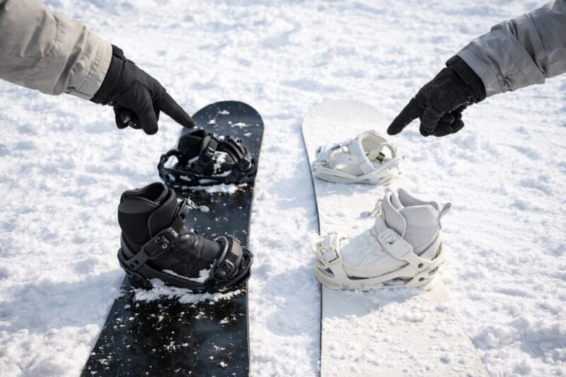 雪の上に並べた2本のスノーボードに、それぞれビンディングとブーツを組み合わせて置き、両側から手で指し示しながら比較している様子。